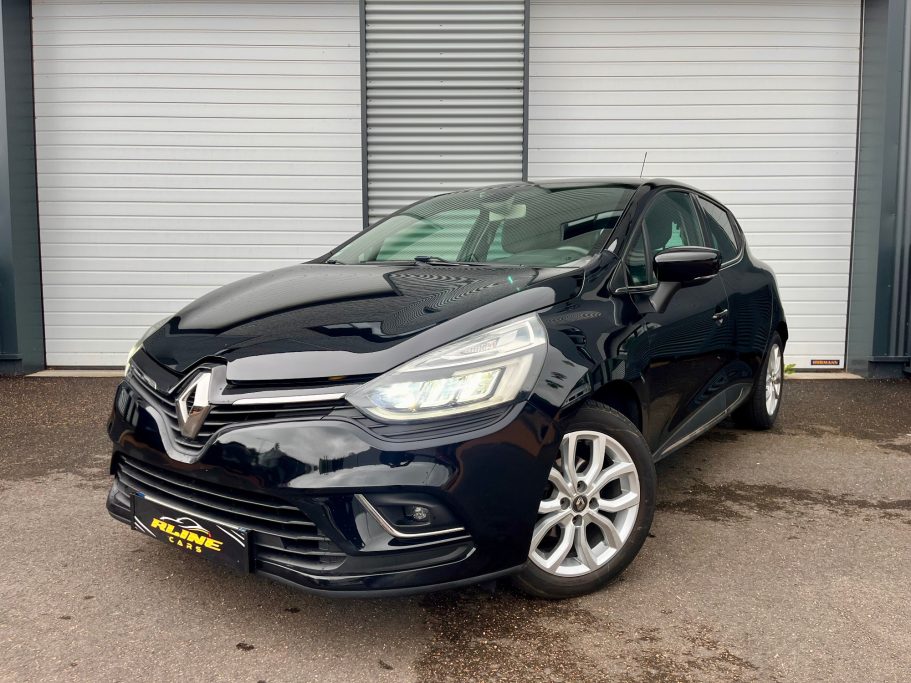 Voiture Renault Clio noire, garée devant un mur avec des rideaux en métal.